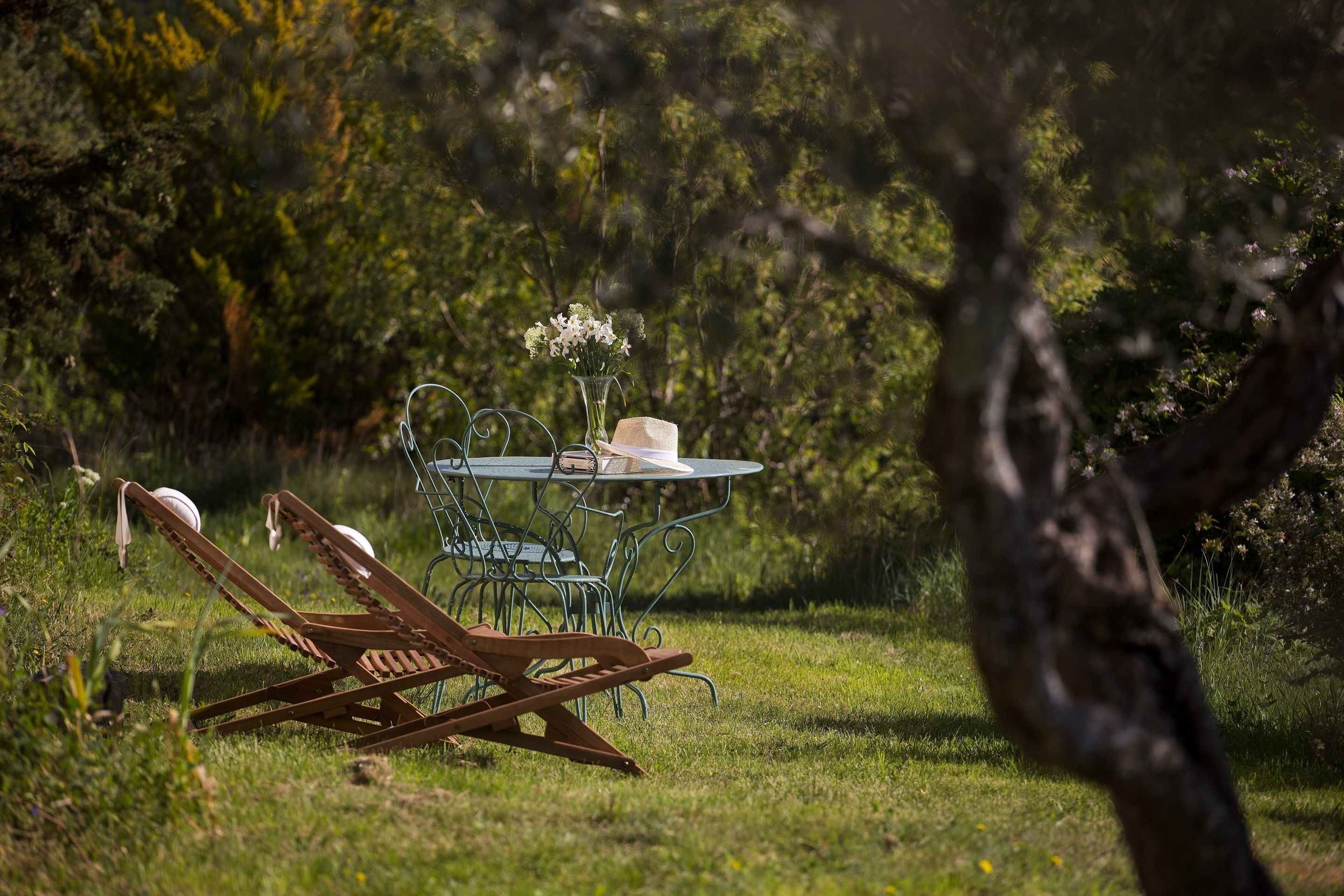A table with a vase of flowers and a hat, surrounded by metal chairs in a grassy outdoor area.