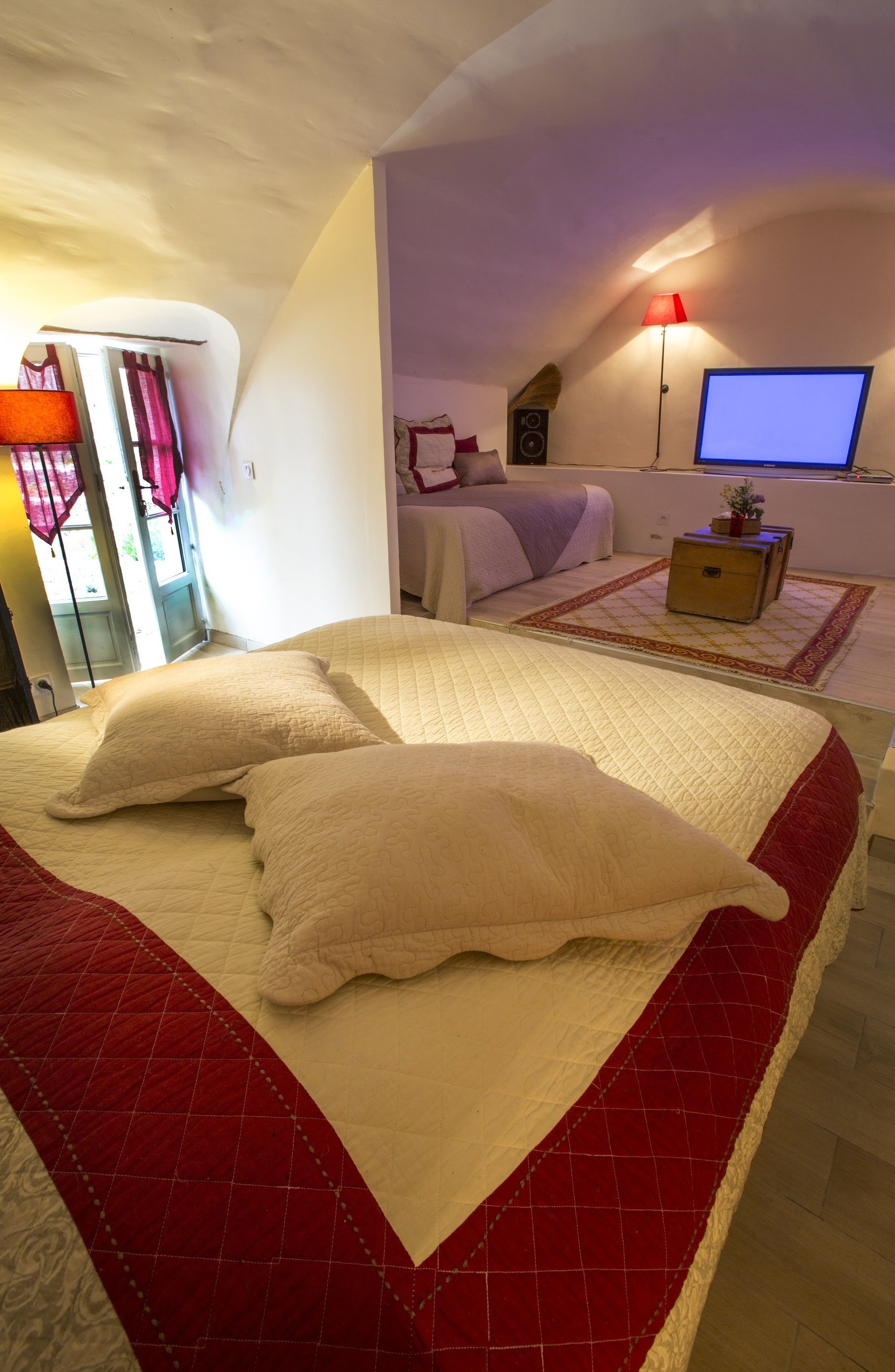 A bedroom with a large bed, a TV, a bedside table, and a window with curtains.