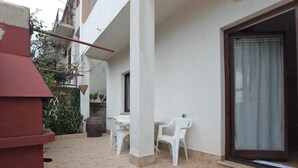 Un espace extérieur aménagé en terrasse, avec une table et des chaises, une grande fenêtre et une structure rouge.