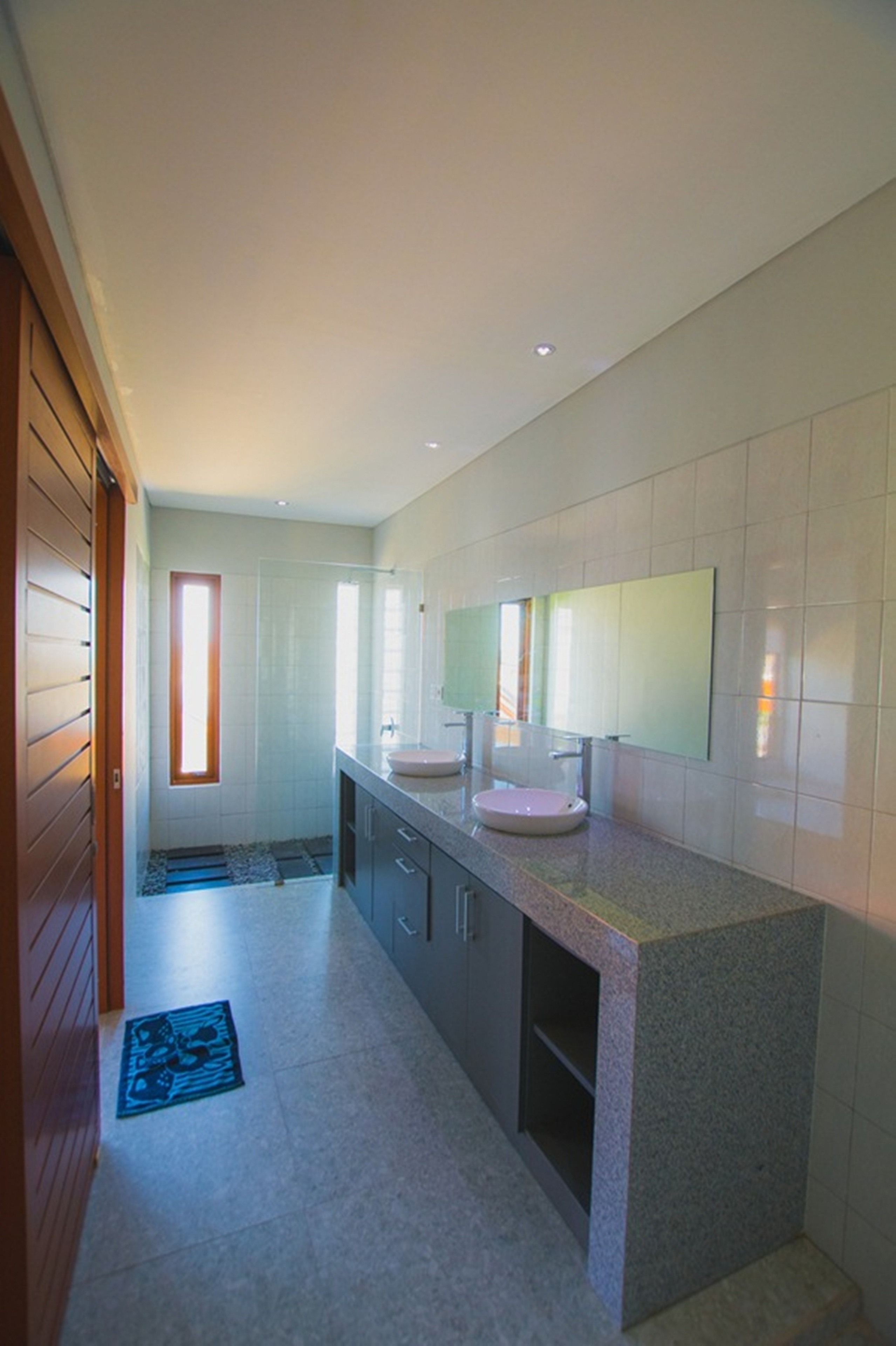 A modern bathroom with a large mirror, two sinks, and a walk-in shower.