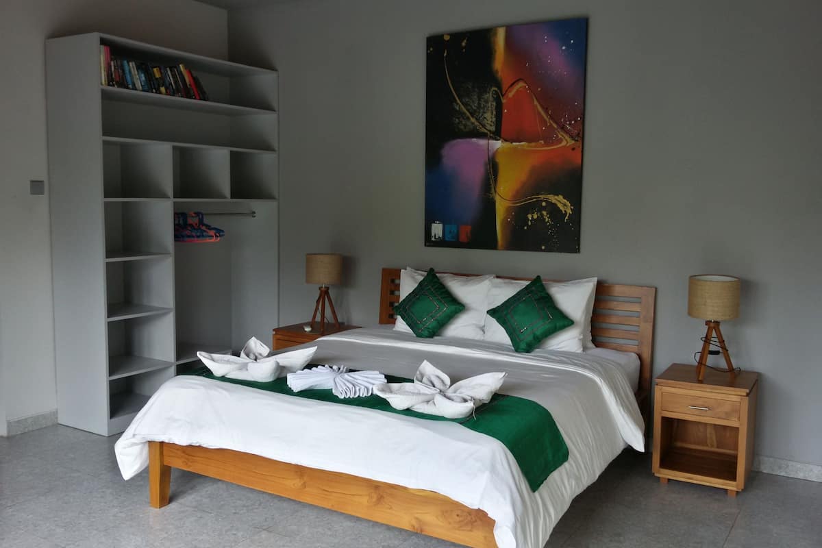 A neatly arranged bedroom with a bed, bedside tables, a bookshelf, and a painting on the wall.