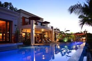 A modern hotel with a swimming pool, a covered outdoor area, and a well-lit interior. - Le Gite du Bonheur (Tamarin)