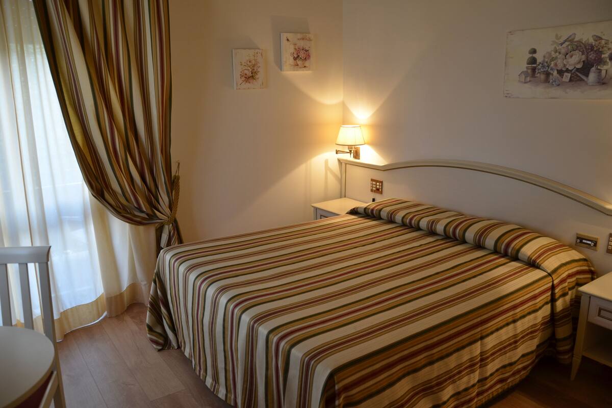 A neatly arranged hotel room with a large bed, a bedside table, a lamp, and a chair.