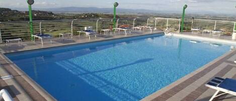 Una piscina con vistas al campo, rodeada de sillas de descanso y una barandilla.