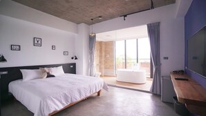 Un dormitorio moderno con una cama grande, un escritorio de madera y un ventanal corredero que da a un balcón.