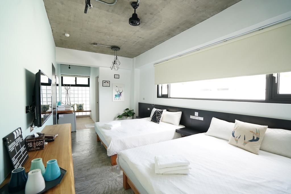 A hotel room with two beds, a desk with a chair, a television, and a large window.