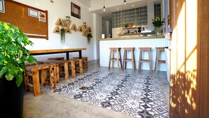 Un café acogedor con mesas y taburetes de madera, un tablón de anuncios con notas y una zona de cocina con taburetes.