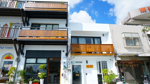 Un edificio moderno con fachada blanca, balcones de madera y plantas en macetas al frente.