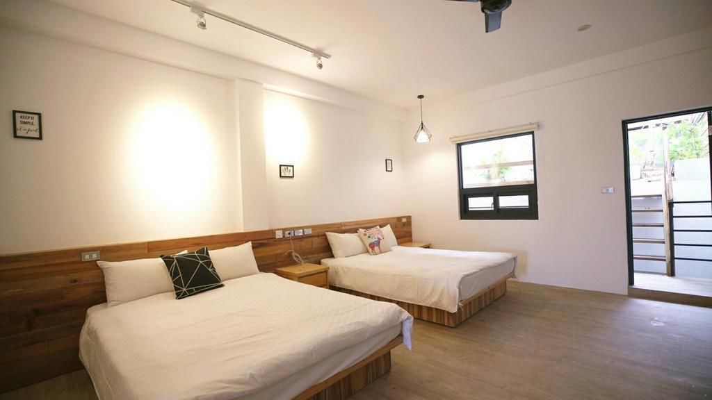 Una habitación con dos camas, cabeceros de madera, un ventanal y una puerta que da al exterior.