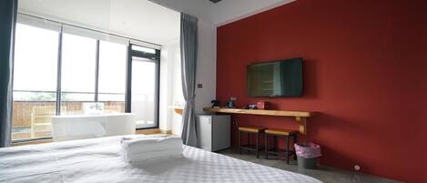 A modern hotel room with a large bed, a small kitchenette, a large window, and a red accent wall.
