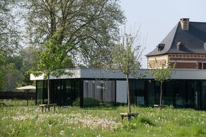 A modern building with large glass windows, surrounded by a grassy field with trees and a bench.