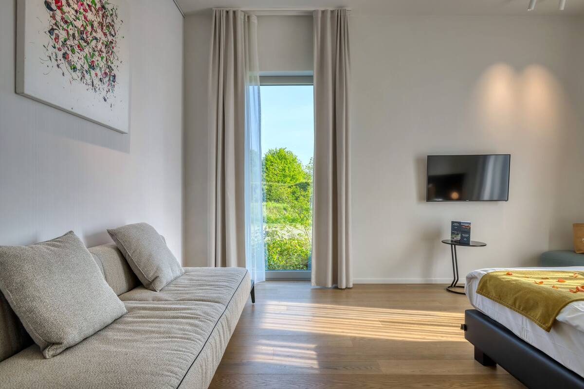 Une chambre moderne avec un canapé, un lit, une télévision et une vue sur la verdure environnante.