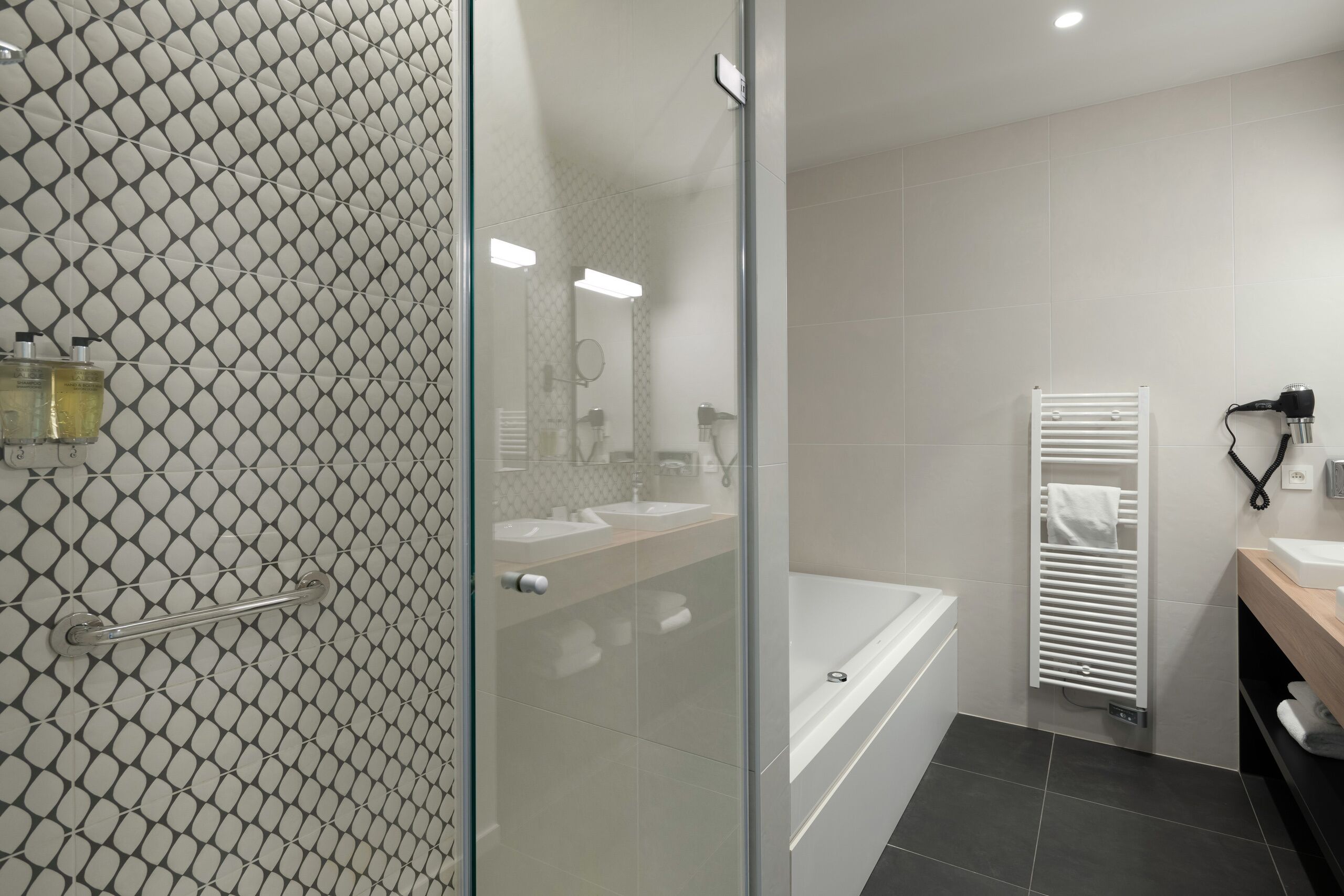 A modern bathroom with a glass shower enclosure, a bathtub, and a vanity with a towel rack.
