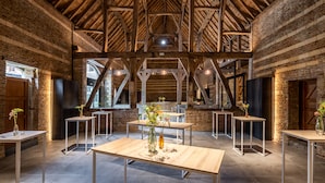 Een interieur met onbehandelde bakstenen muren, houten balken en moderne tafels met vazen.