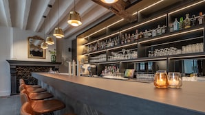 Een bar met een lange toonbank, diverse flessenkasten en een rij barstoelen.