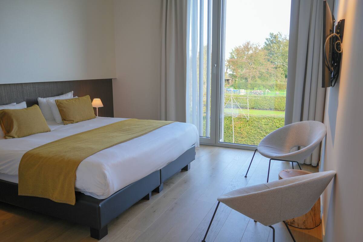 Une chambre d’hôtel moderne avec un grand lit, un fauteuil et une vue sur l’extérieur.