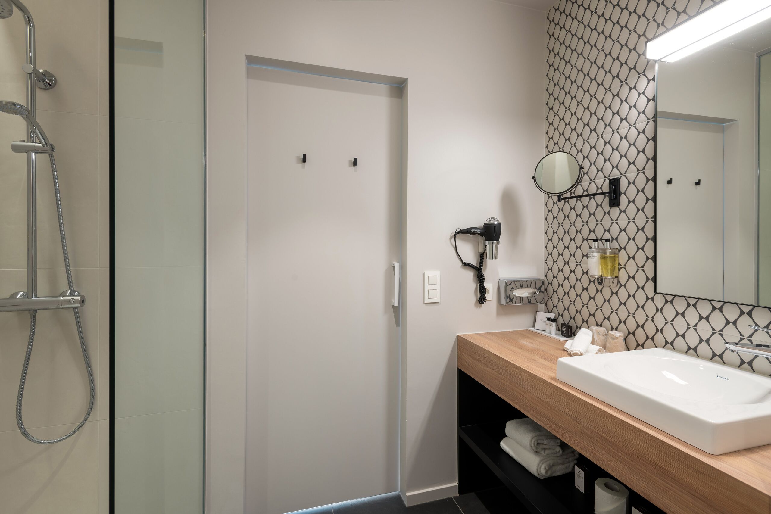 A modern bathroom with a glass shower enclosure, a wooden vanity with a white sink, and a mirror.