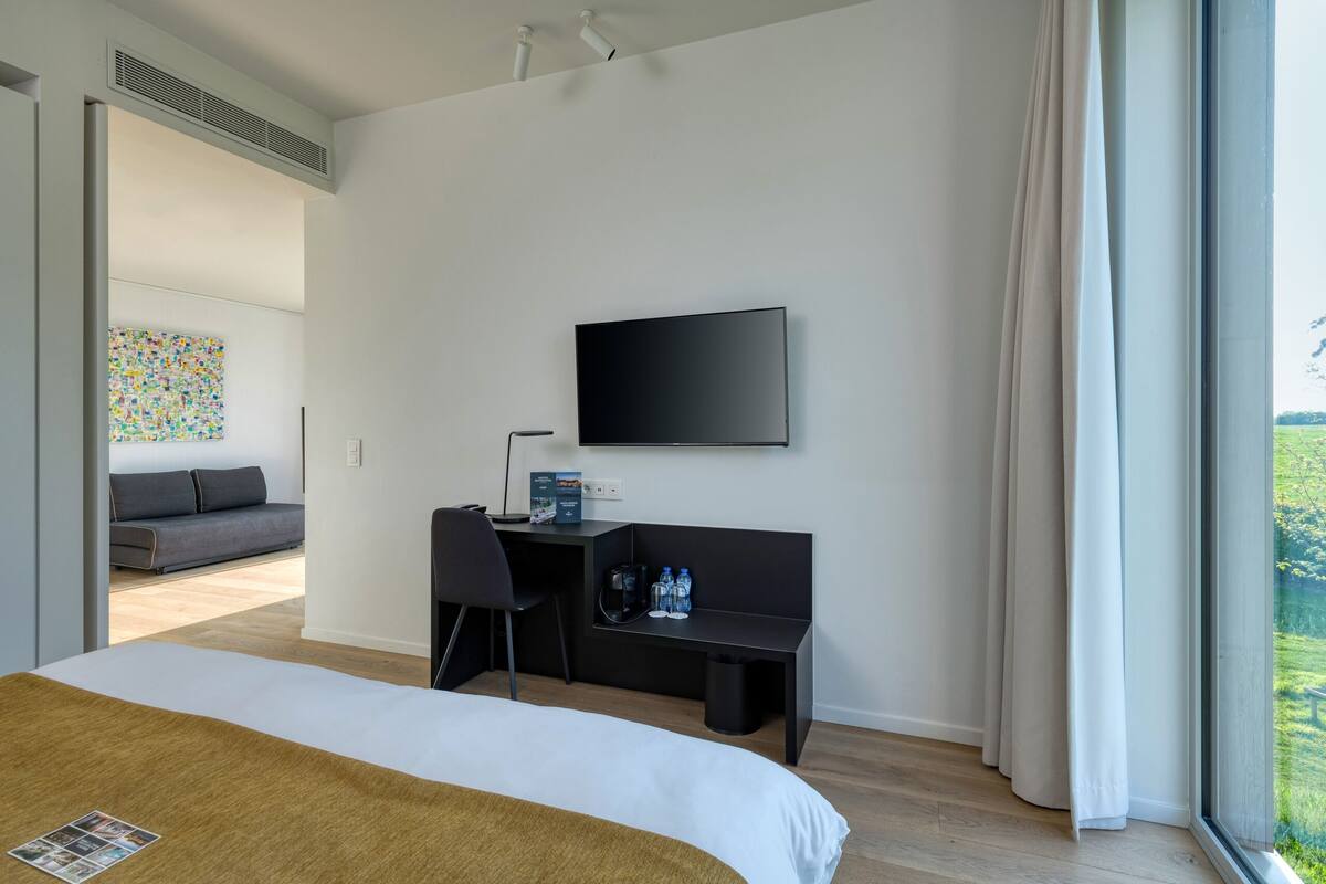 Une chambre d’hôtel moderne dotée d’un grand lit, d’un bureau avec une chaise, d’un téléviseur à écran plat et d’une fenêtre avec des rideaux.