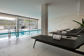 A modern indoor pool area with lounge chairs and a sunbed.