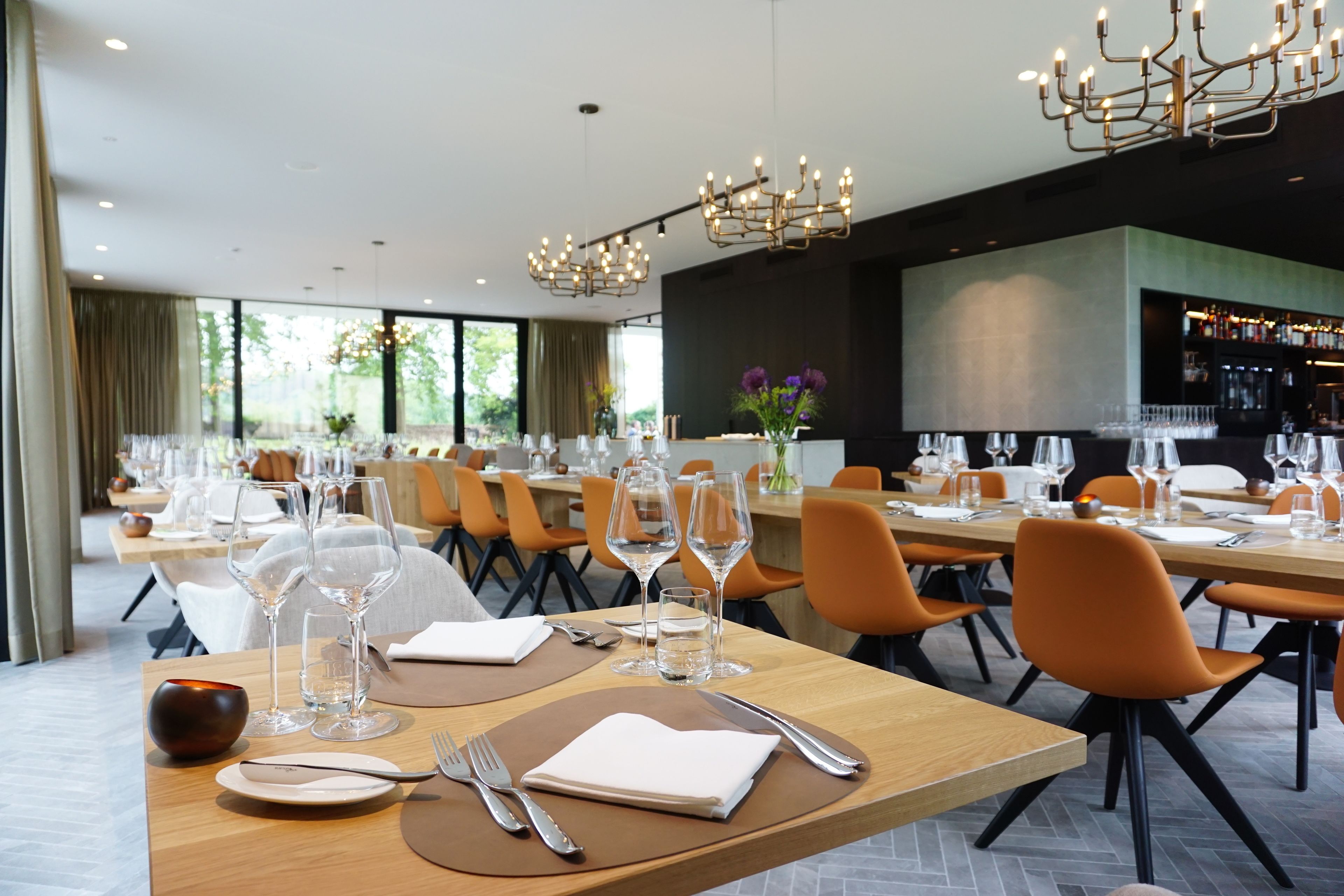 A restaurant with multiple dining tables, each set with plates, cutlery, and wine glasses.
