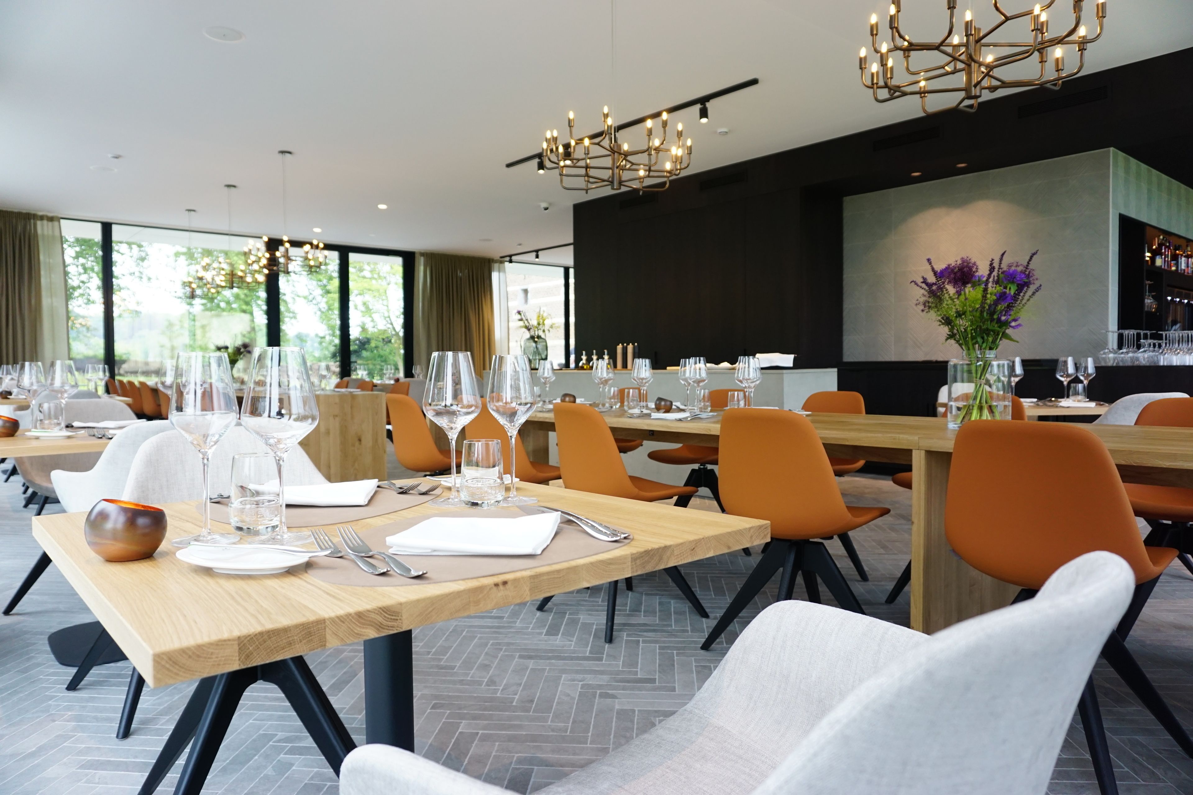 A modern dining area with wooden tables, orange chairs, and a chandelier.