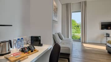 Een moderne hotelkamer met een houten vloer, een bank, een bureau met een koffiezetapparaat, waterflessen en een televisie.
