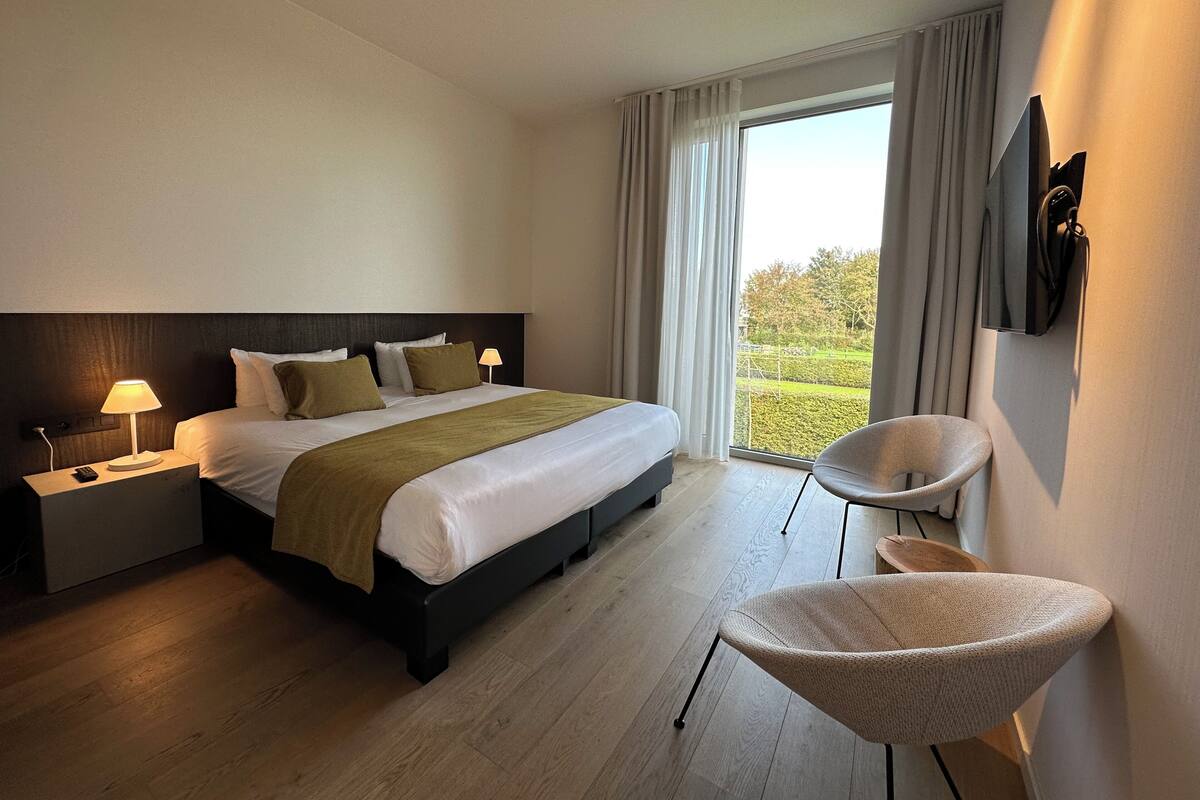 Une chambre d’hôtel moderne, dotée d’un grand lit, de lampes de chevet, d’une télévision et offrant une vue sur l’extérieur.