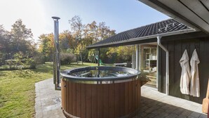 Et træspabad i en baghave med et pergolaoverdækket område, gyngestativ og en overdækket terrasse.