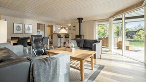 En moderne stue med træloft, pejs, spiseområde med bord og stole, samt en stor skydedør til en have.
