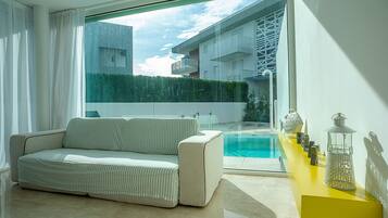 A modern living room with a sofa, a yellow side table, and a view of a swimming pool and buildings outside.