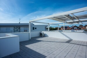 Terraza en la azotea con pérgola, un pequeño equipo de aire acondicionado y vistas a edificios cercanos.