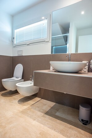 Un baño moderno con un bidé, un lavamanos grande y un espejo.