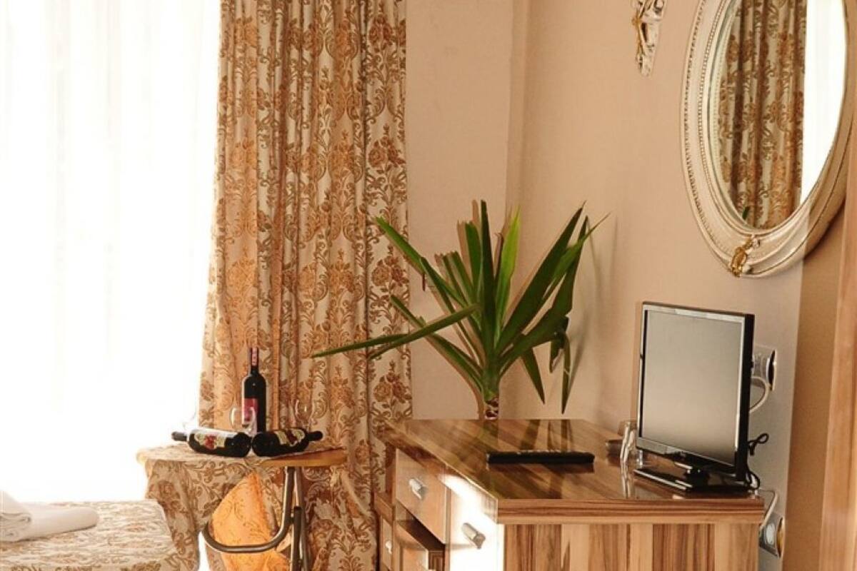 A hotel room with a bed, a desk with a computer, a potted plant, and a mirror.