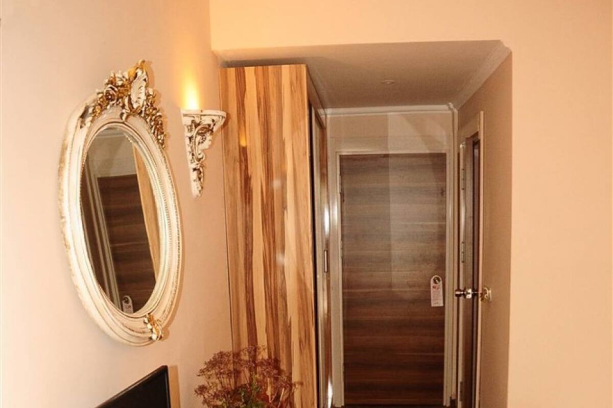 A hotel room with a wooden desk, a television, a mirror, a bed with towels, and a patterned carpet.