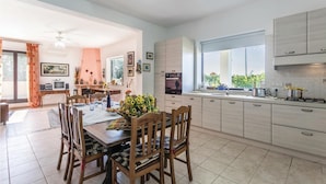 A spacious kitchen with modern appliances, a dining area with wooden furniture, and a view of greenery outside. - Villa Betty (Ragusa -RG-)