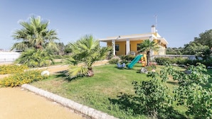 A yellow building with a covered patio and a slide, surrounded by greenery and a clear sky. - Villa Betty (Ragusa -RG-)