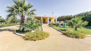 A modern house with a yellow facade, a front porch, and a garden with palm trees and yellow flowers. - Villa Betty (Ragusa -RG-)