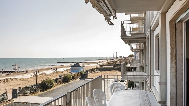 A balcony with a view of the beach, white plastic chairs, and a table. - Helvezia (Jesolo)