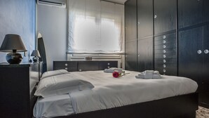 A modern bedroom with a large bed, a dresser, a mirror, and a wardrobe with multiple compartments. - Helvezia (Jesolo)