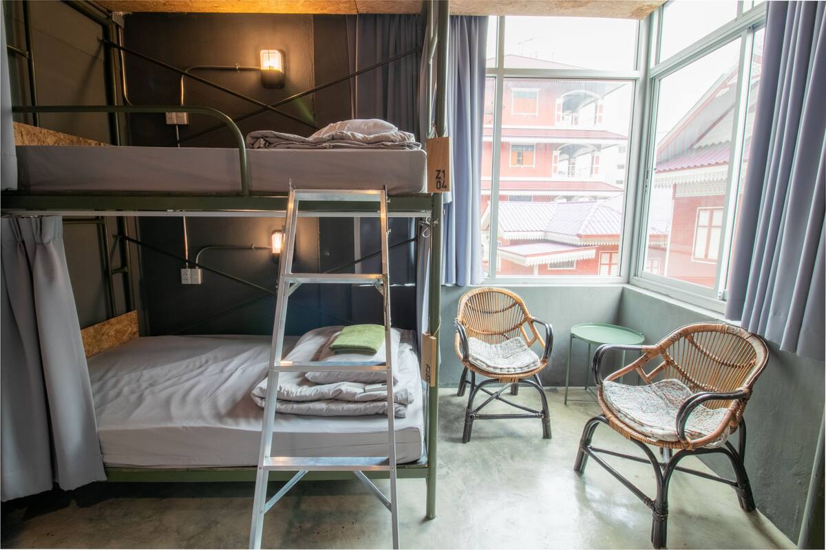 A bunk bed room with a ladder, two wicker chairs, and a small table.