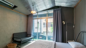 A bedroom with a large bed, a bench, and a window with curtains. - Zhelter'BKK - Hostel (Bangkok)