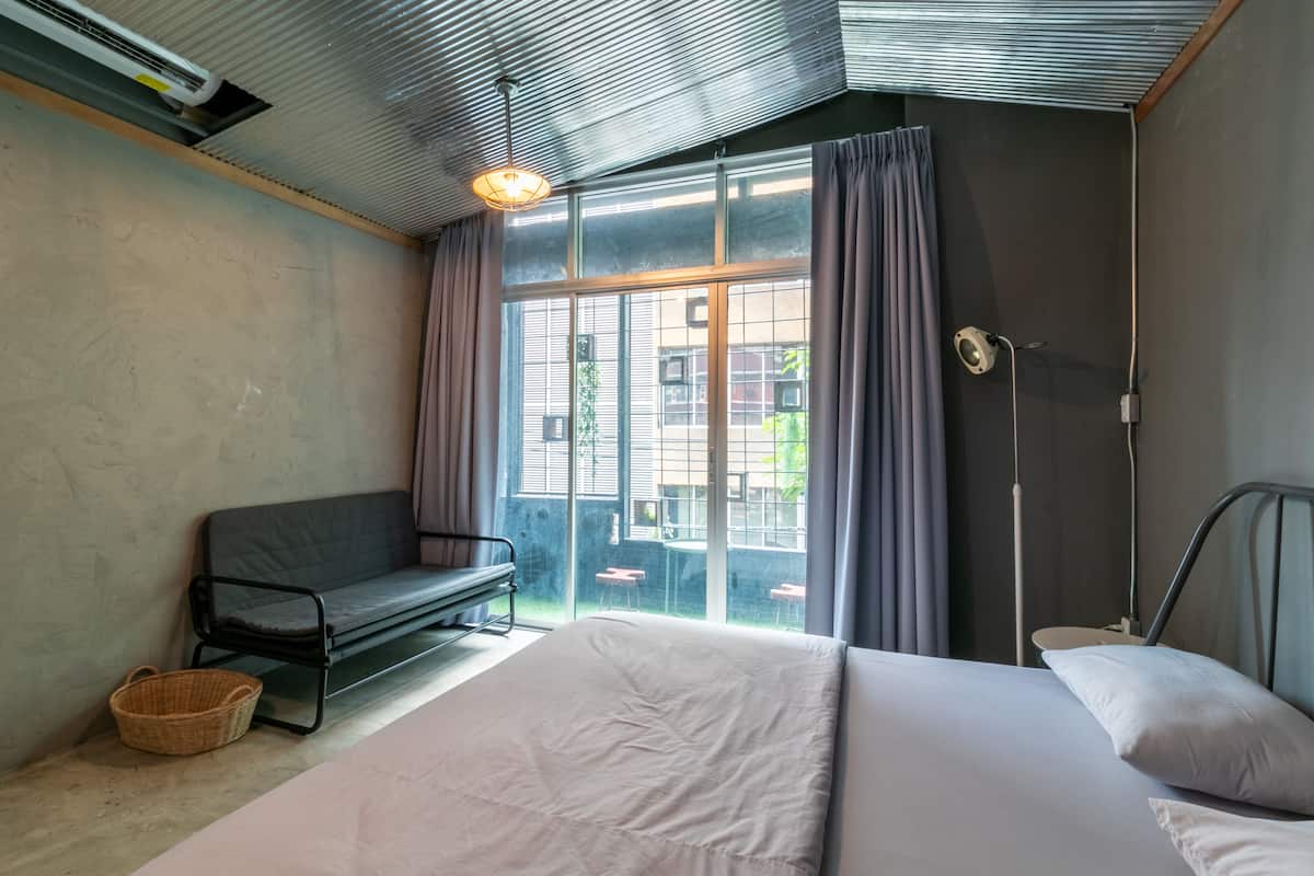 A bedroom with a large bed, a bench, and a window with curtains.