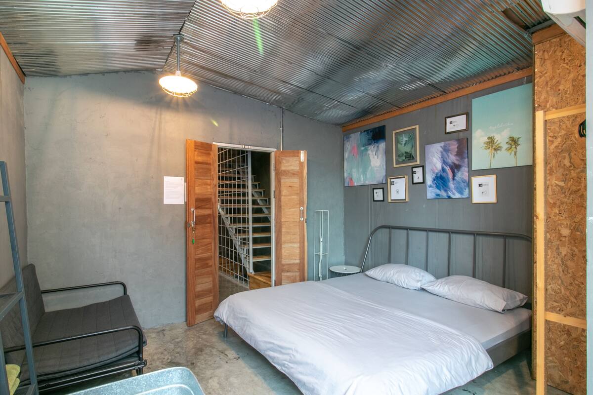 A bedroom with a bed, a chair, a wardrobe, and a door leading to a staircase.