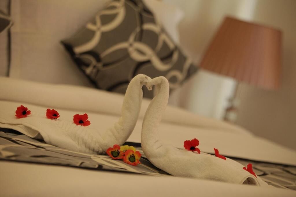 Una cama bien hecha con una toalla dispuesta en forma de corazón, un par de zapatos y flores rojas.
