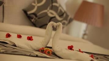Una cama bien hecha con una toalla dispuesta en forma de corazón, un par de zapatos y flores rojas.