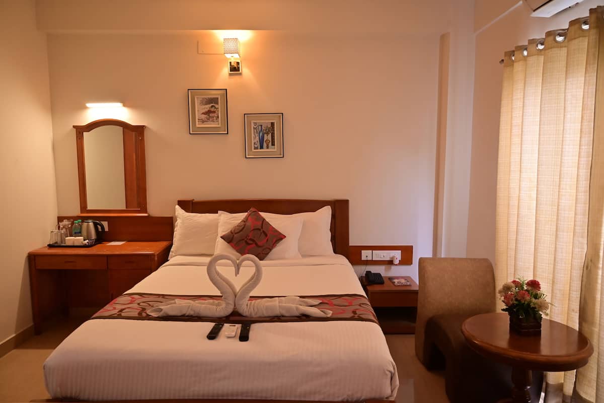 Una habitación de hotel con una cama bien hecha, una mesita de noche con una lámpara, una silla y una pequeña mesa con un jarrón de flores.