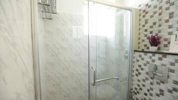 Un baño con cabina de ducha de vidrio, pared de mármol y salpicadero de azulejos.