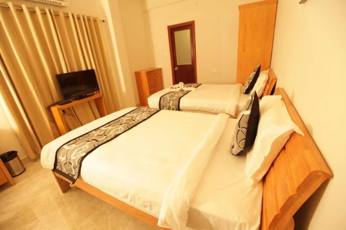 Habitación de hotel con dos camas, un televisor sobre una mesita, un armario de madera y una puerta con espejo.