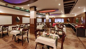 A spacious dining area with multiple tables and chairs, a buffet line, and a large screen on the wall.