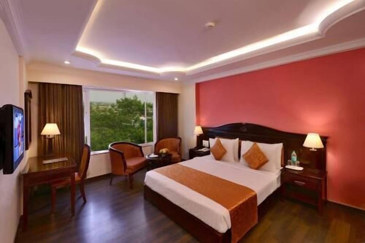 A hotel room with a large bed, two bedside tables, a chair, a TV, and a window with a view.